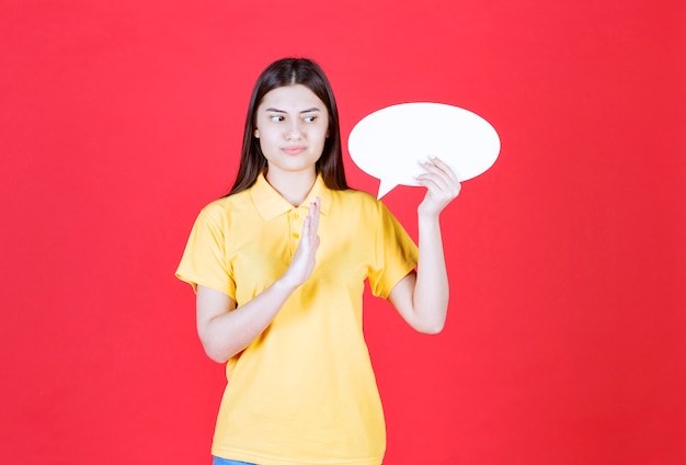 Menina com dresscode amarelo segurando um quadro oval de informações e parando alguém