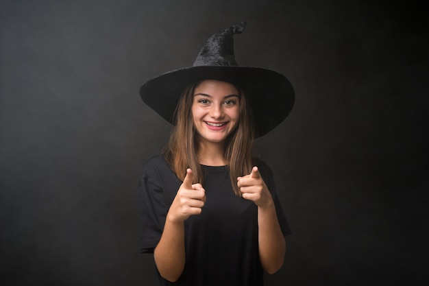 Foto menina com fantasia de bruxa para festas de halloween sobre dedo de pontos de parede escura isolado para você