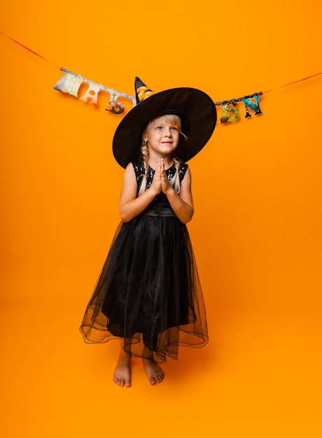 Foto menina com fantasia de halloween preto rindo e olhando para a câmera, pulando e se divertindo, isolado no fundo amarelo. dia das bruxas
