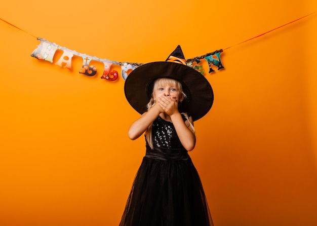 Menina com fantasia de halloween preto rindo e olhando para a câmera, pulando e se divertindo, isolado no fundo amarelo. dia das Bruxas