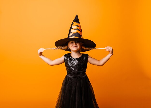 Menina com fantasia de halloween preto rindo e olhando para a câmera, pulando e se divertindo, isolado no fundo amarelo. dia das Bruxas