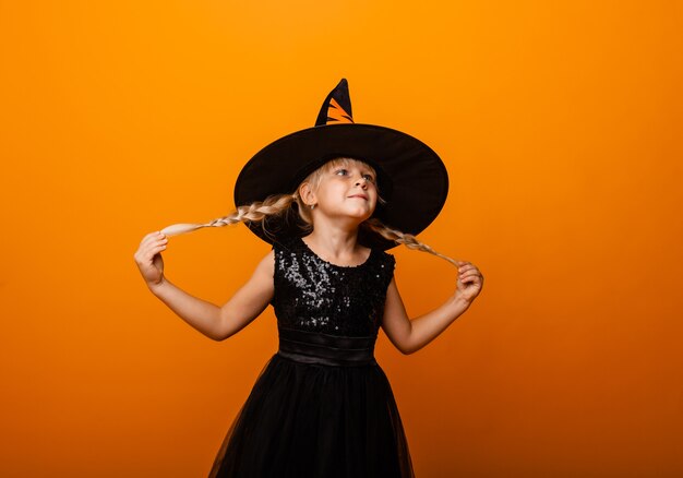 Menina com fantasia de halloween preto rindo e olhando para a câmera, pulando e se divertindo, isolado no fundo amarelo. dia das Bruxas