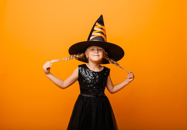 Menina com fantasia de halloween preto rindo e olhando para a câmera, pulando e se divertindo, isolado no fundo amarelo. dia das Bruxas