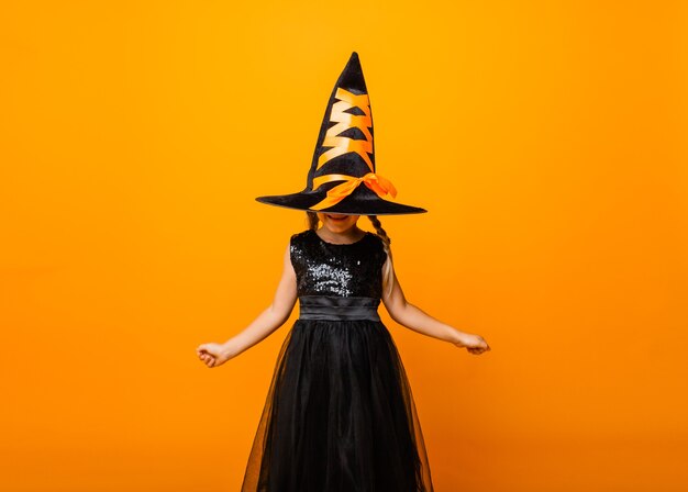 Foto menina com fantasia de halloween preto rindo e olhando para a câmera, pulando e se divertindo, isolado no fundo amarelo. dia das bruxas