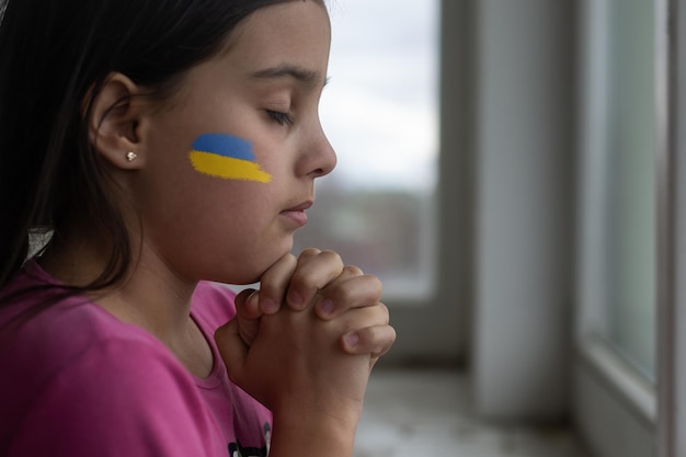 Menina com fita de bandeira ucraniana rezando o símbolo da paz e rezando pela Ucrânia