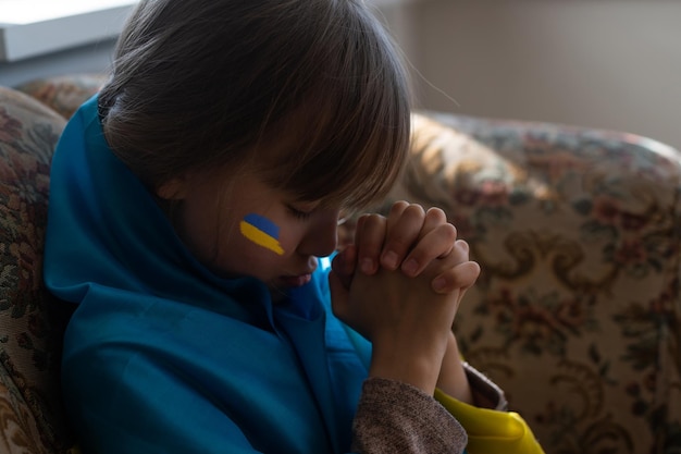 Menina com fita de bandeira ucraniana rezando o símbolo da paz e rezando pela ucrânia