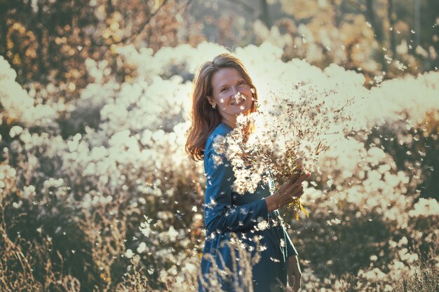 Menina com flores contra o sol da tarde de outono. penugem de dente de leão no parque outono.