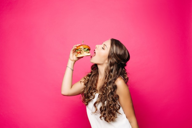 Menina com fome com a boca aberta, comendo hambúrguer grande.