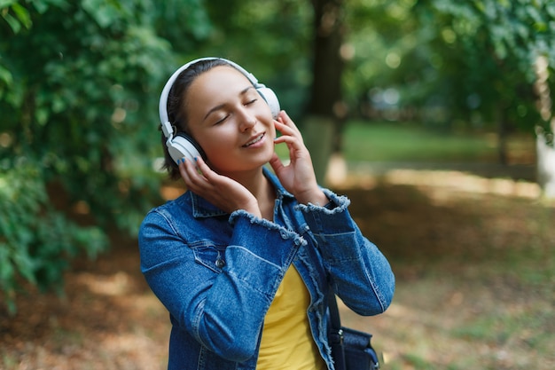 Menina com fones de ouvido, passear no parque em um dia ensolarado e ouvir música