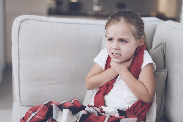 Foto menina com frio tem dor de garganta no sofá.