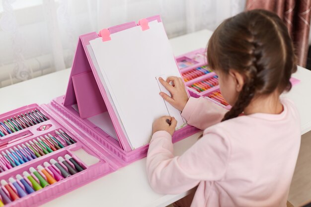 Menina com giz de cera desenhando uma foto sentada à mesa
