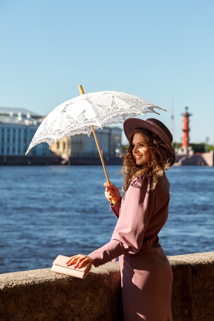 Menina com guarda-chuva branco. Mulher bonita com um guarda-chuva do sol. Mulher jovem atraente carregando um guarda-chuva e sorrindo em pé na rua. Mulher feliz com um guarda-chuva. Caminhe no Parque