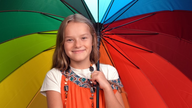 Menina com guarda-chuva colorido do arco-íris nas mãos com um vestido laranja em pé feliz
