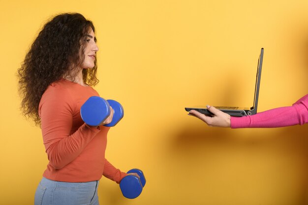 Menina com guiador pronto para iniciar o ginásio online com um computador. parede amarela