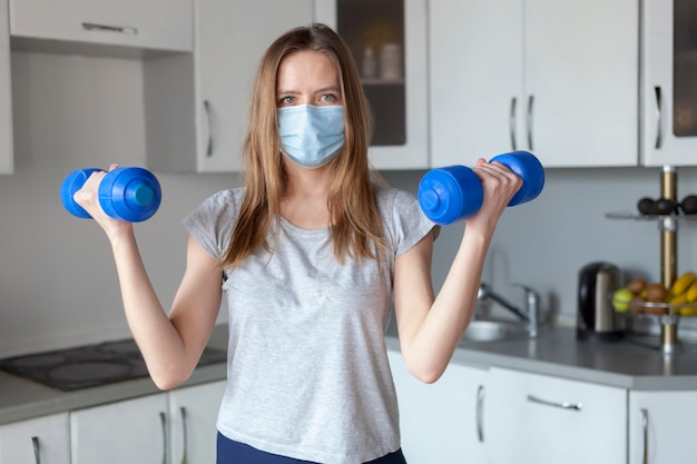 Menina com halteres na cozinha usando máscara protetora