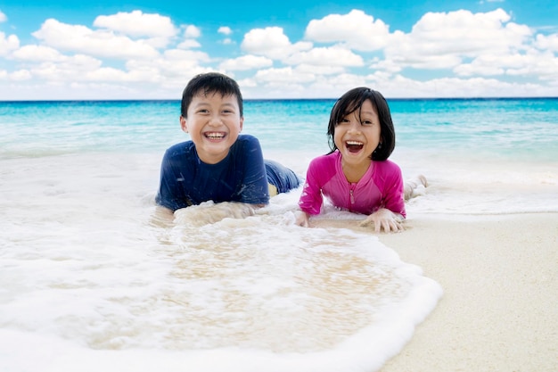 Menina com irmão a brincar de ondas na praia.
