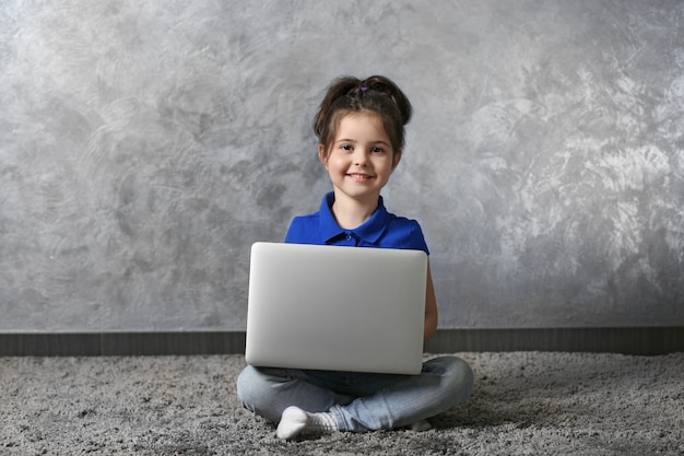 Menina com laptop no tapete de pele contra a parede cinza