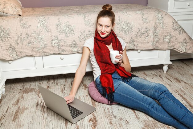 Menina com laptop sentada no chão e bebendo