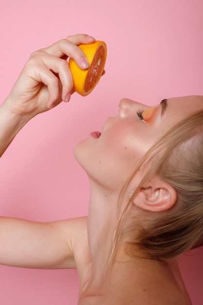 Menina com laranja em uma parede rosa