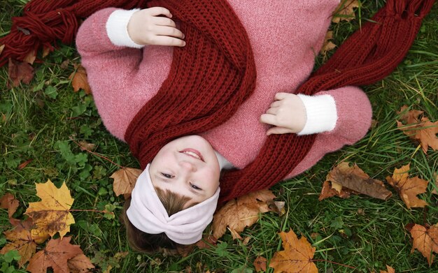 Menina com lenço vermelho sorrindo deitada na grama com folhas de plátano