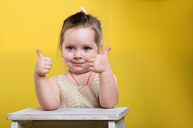 Menina com lindo vestido com cadeira em fundo amarelo