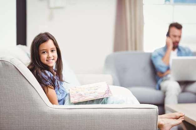 Menina com livro de imagens enquanto pai em segundo plano