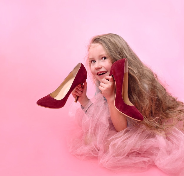 menina com longos cabelos loiros em saia rosa com sapatos de salto alto vermelho da mãe brincando de adulto