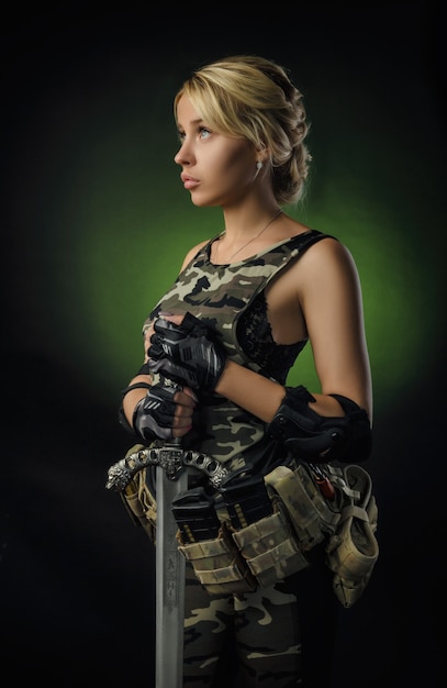 Menina com macacão militar de airsoft posando com uma arma nas mãos em um fundo escuro