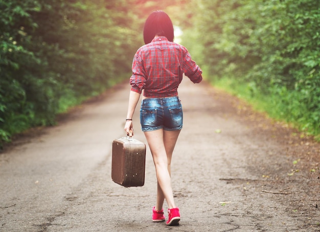 Menina com mala vintage é asfalto. garota viajando pedindo carona.