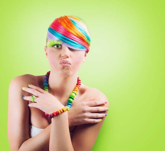 Menina com maquiagem colorida de moda arco-íris sobre fundo verde.