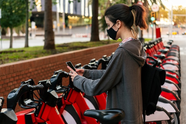 Menina com máscara desbloqueando uma bicicleta com o telefone