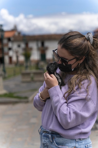 Menina com máscara facial abraçando um cachorro de rua na rua