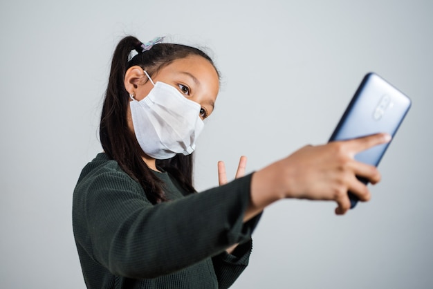 Menina com máscara médica no rosto tirando uma selfie