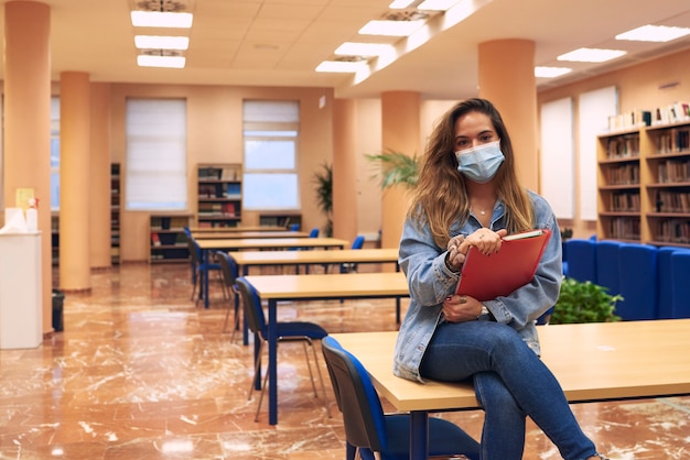 Menina com máscara olha para a câmera com uma biblioteca vazia ao fundo