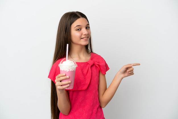 Menina com milk-shake de morango sobre fundo branco isolado apontando o dedo para o lado