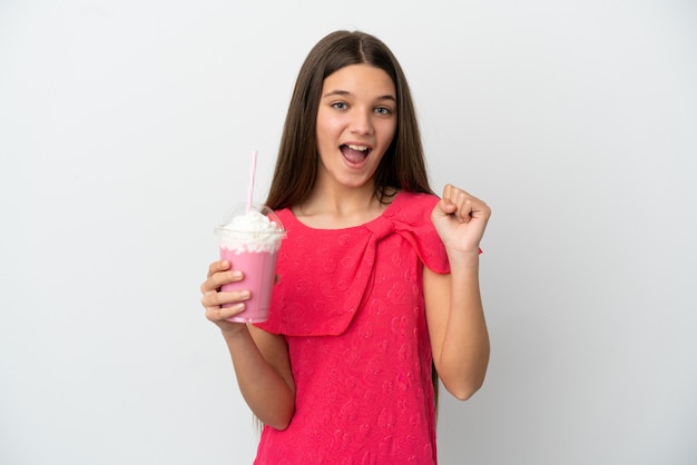 Menina com milk-shake de morango sobre fundo branco isolado comemorando vitória na posição de vencedor