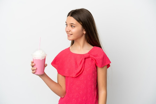 Menina com milk-shake de morango sobre fundo branco isolado, olhando para o lado