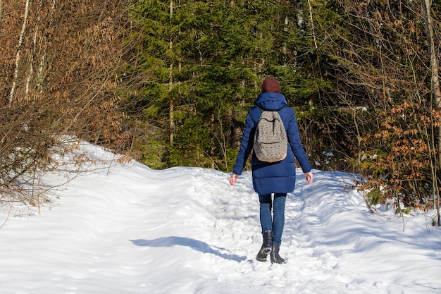 Menina com mochila andando em uma floresta de neve Dia ensolarado de inverno