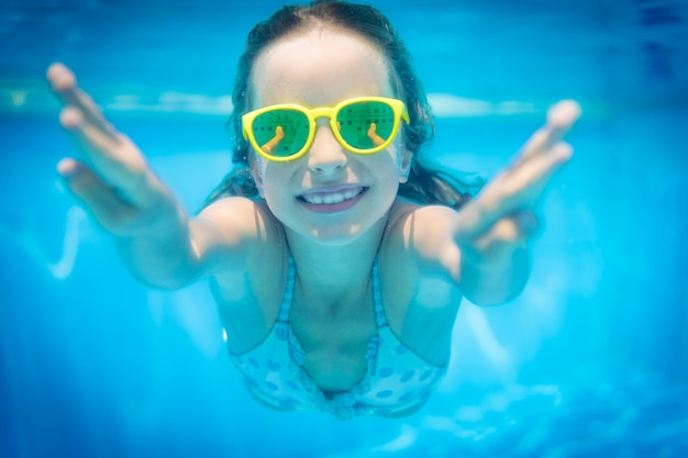 Menina com óculos amarelos debaixo d'água na piscina