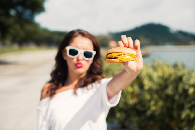 Menina com óculos de sol, mostrando um hambúrguer