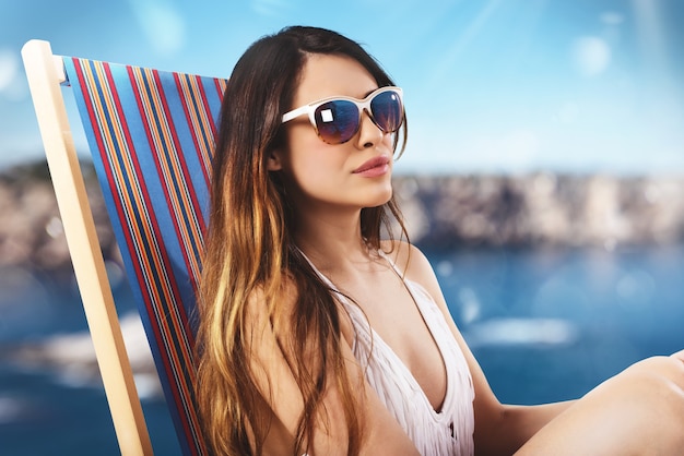 Menina com óculos de sol na espreguiçadeira na praia