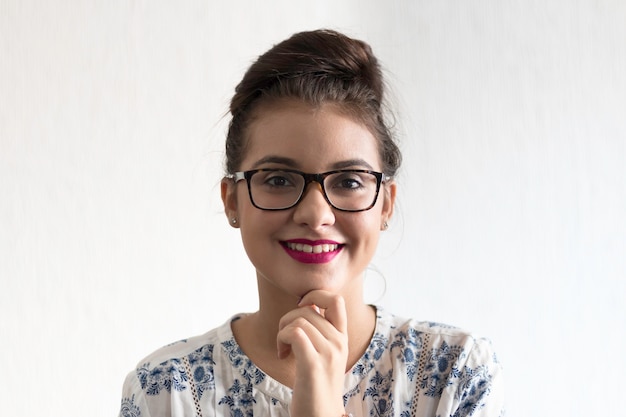 Menina com óculos e mão no queixo com fundo branco.