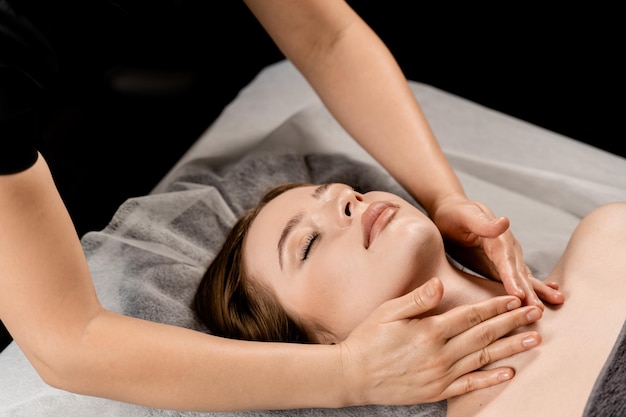 Menina com olhos fechados está relaxando na massagem de rosto e pescoço no spa Massagista está fazendo massagem facial para jovem no spa Facebuilding e procedimentos relaxantes