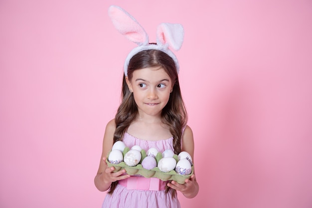 Menina com orelhas de coelho da Páscoa e uma bandeja de ovos nas mãos em um fundo rosa do estúdio. Conceito de férias da Páscoa.