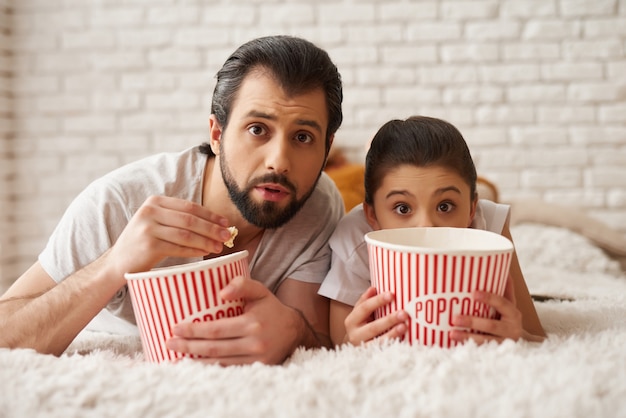 Foto menina com pai assistir filme assustador e comer pipoca.