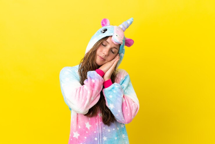 Foto menina com pijama de unicórnio em um fundo isolado fazendo gestos para dormir em expressão dorível