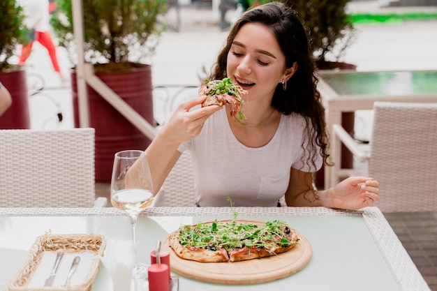 Menina com pinsa romana no café na esplanada. Mulher jovem comendo pinsa e bebendo vinho.