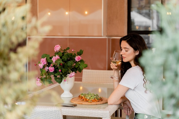 Menina com pinsa romana no café na esplanada. Mulher jovem comendo pinsa e bebendo vinho.