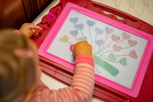 Menina com prato de desenho desenha corações e forma de árvore na mesa. Fundo bonito das crianças