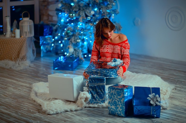 menina com presentes de natal adulto/jovem menina adulta, modelo no interior de ano novo, desembala presentes de natal no pacote